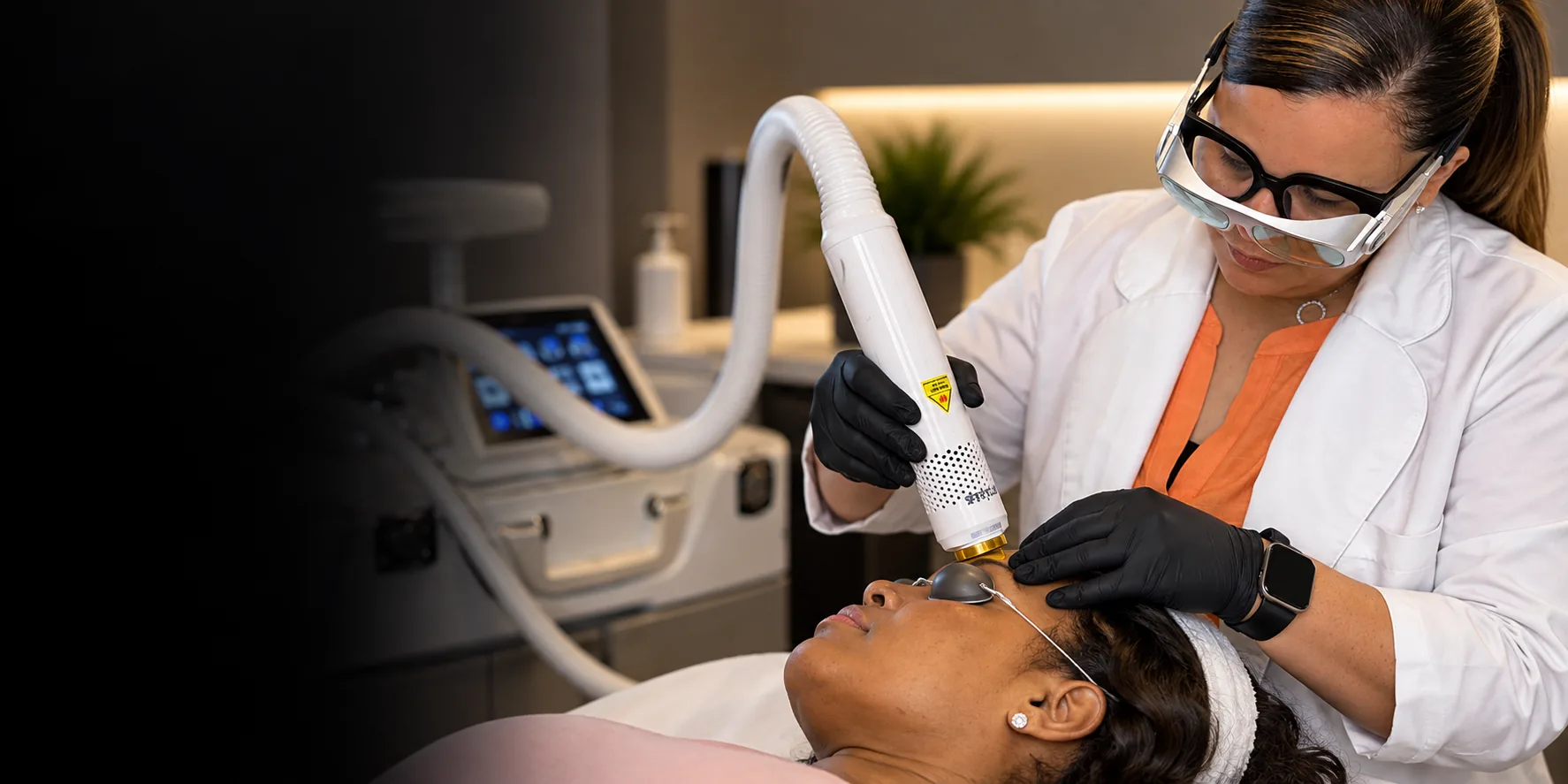Practitioner in laser safety goggles treating a reclining client with an Aerolase handpiece, fading into black on the left